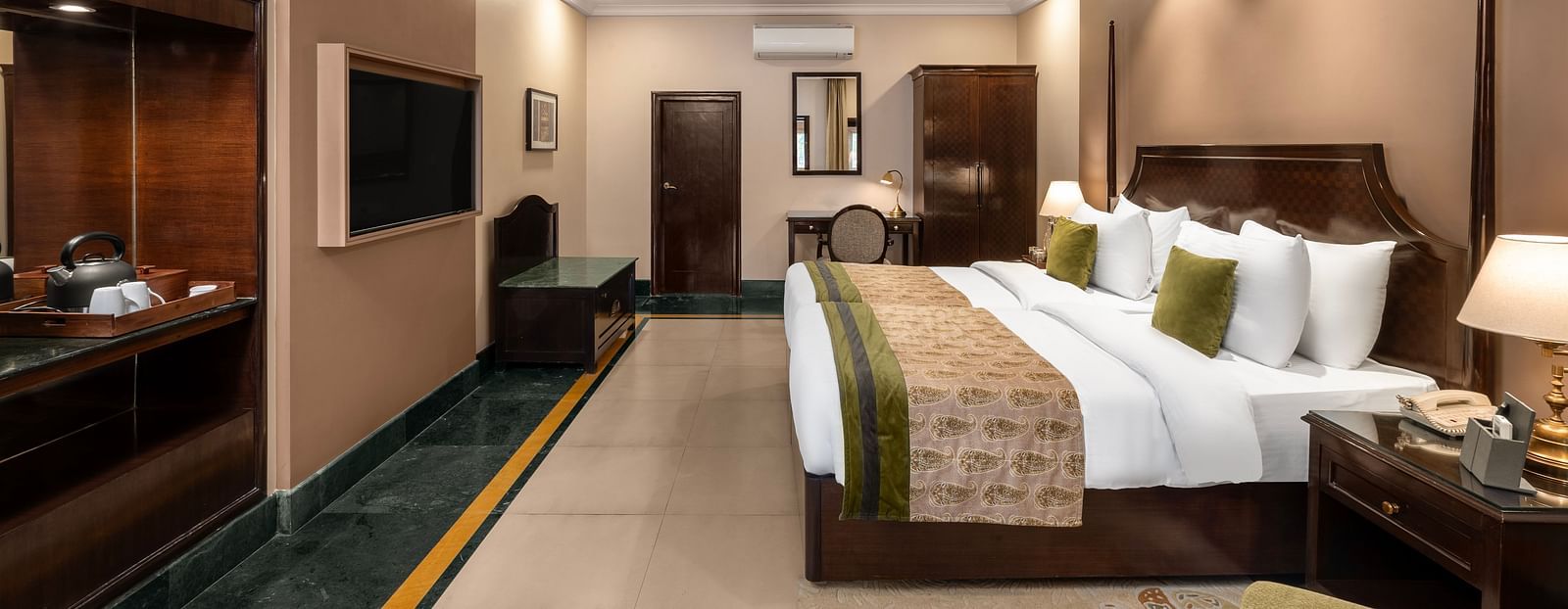 Ganga View Room with a side drawer and side lamp, a workdesk and a large bed facing a television - Ganga Lahari, Haridwar