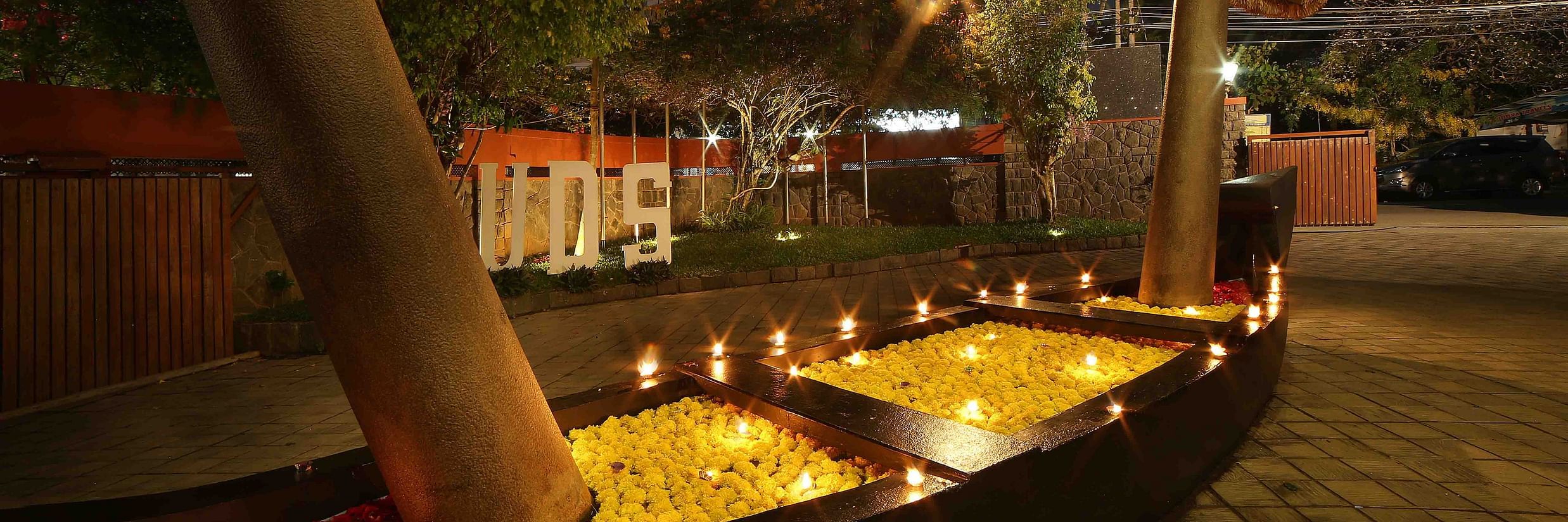 A decorative boat filled with yellow and red flower petals and candles illuminates the outdoor area of Uday Samudra Leisure Beach Hotel at night