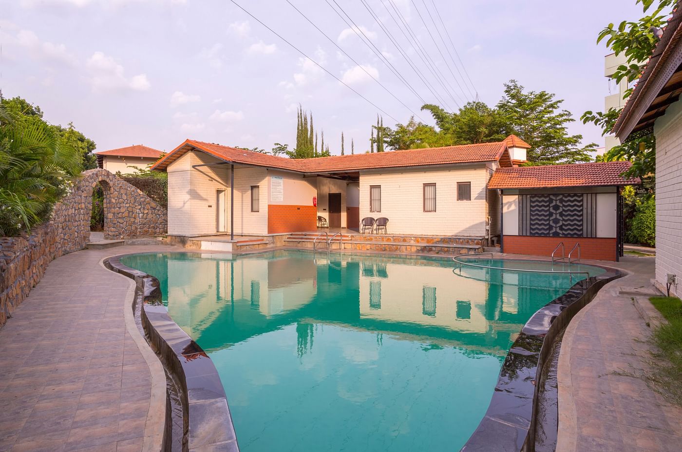 Outdoor swimming pool with cottages in the background – Nirantara Resort & Spa