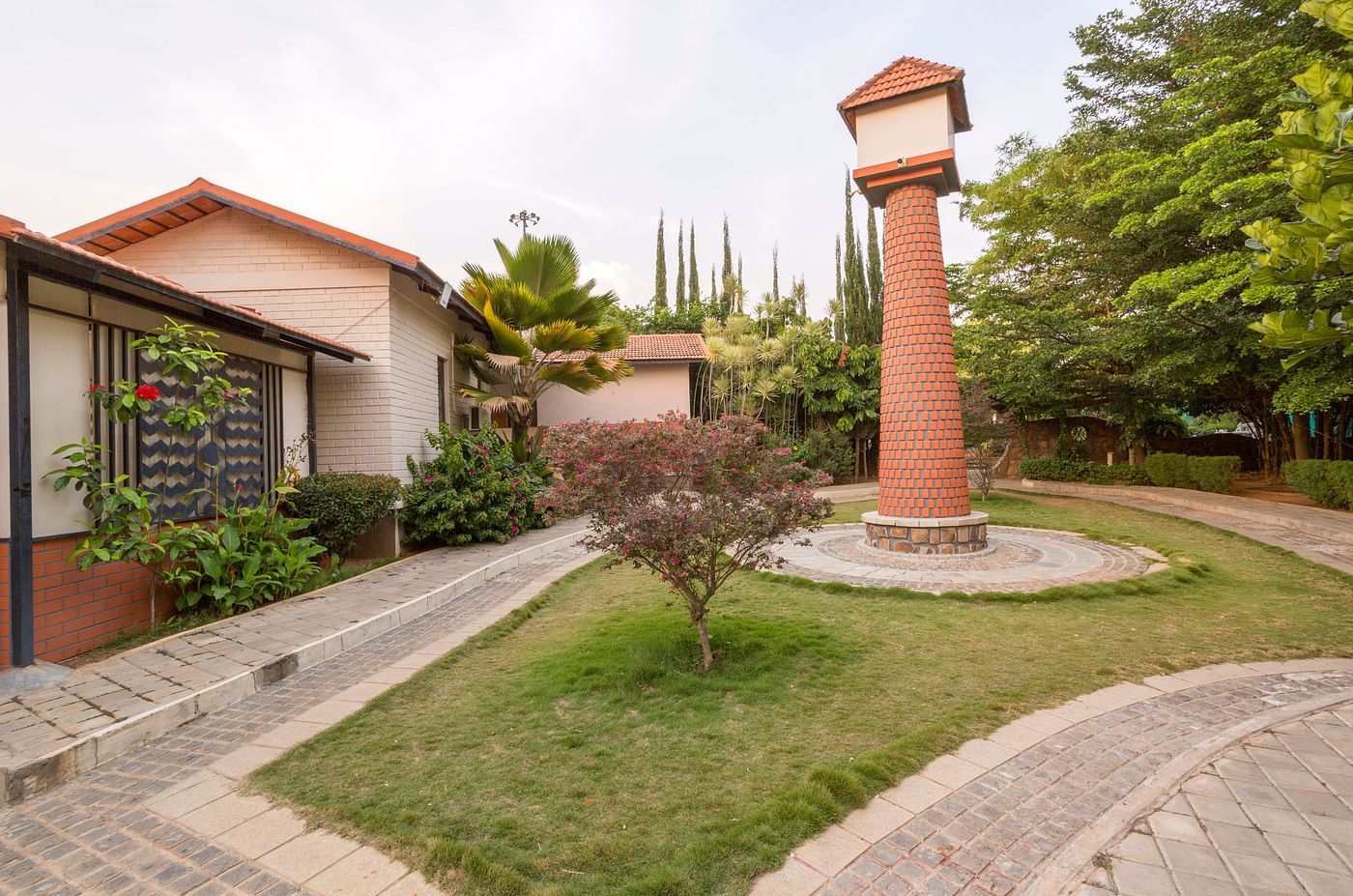 Lush garden with pathway and central pillar near cottages at Nirantara Resort