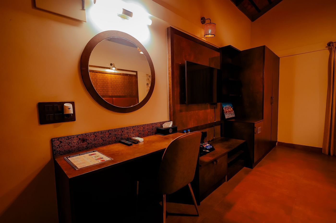 A room with a desk, mirror, and a partially visible bed at Nirantara Resort & Spa.