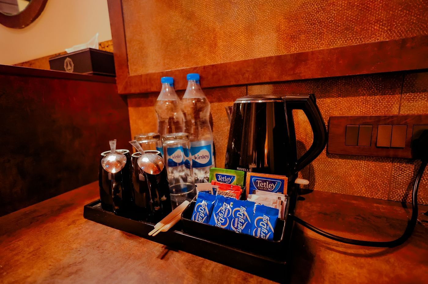 A close-up of a tray with a kettle, bottled water, and small snacks in a dimly lit setting  - Nirantara Resort & Spa.