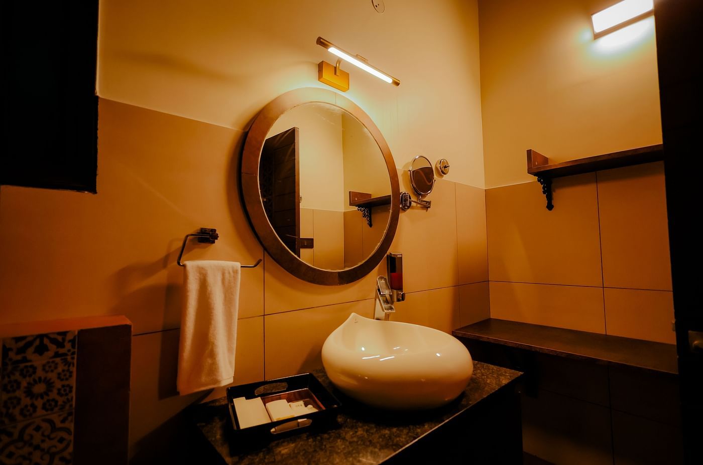 A modern bathroom with a round mirror and a white sink at Nirantara Resort & Spa
