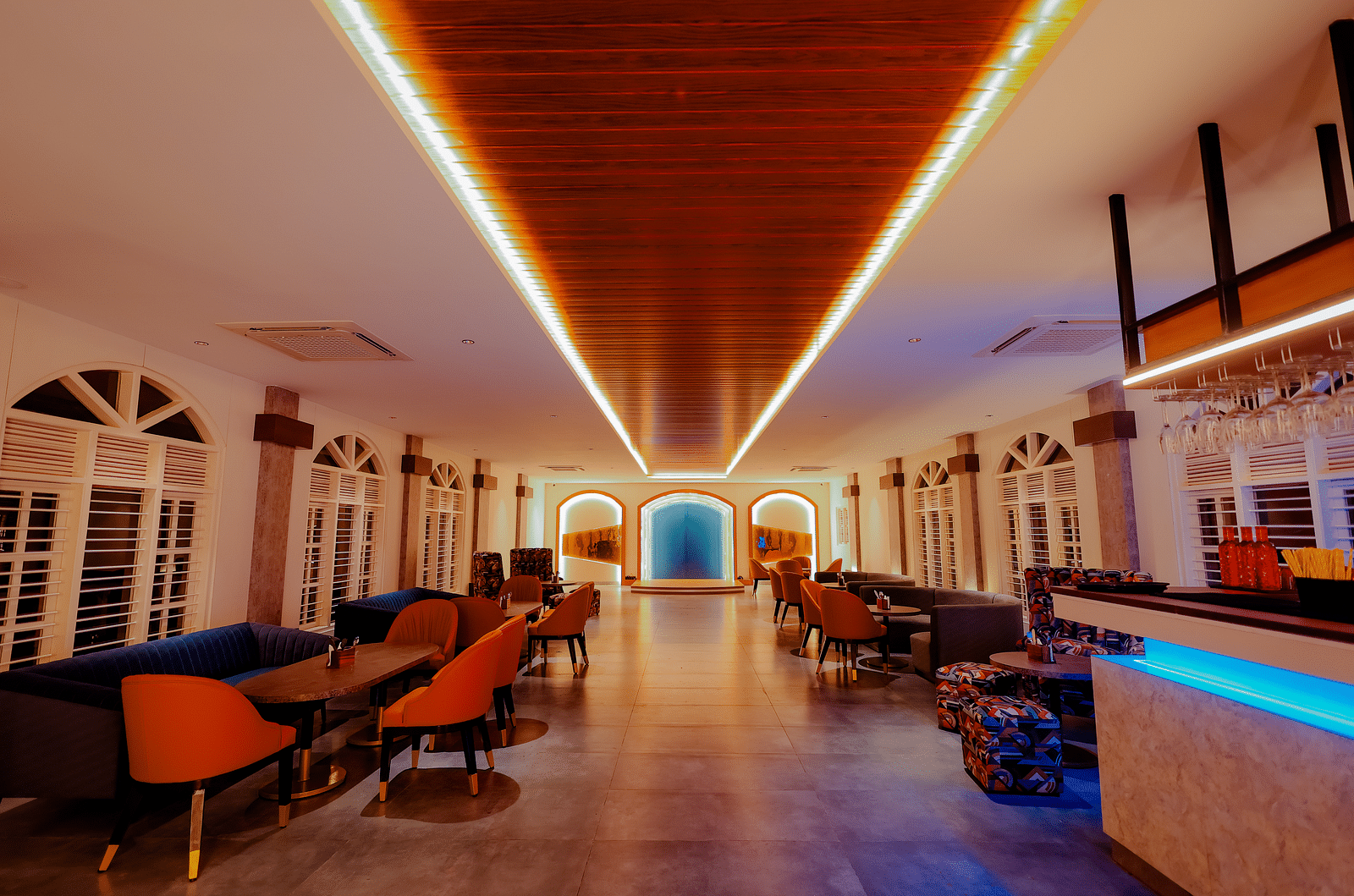 A long, brightly lit hallway with a bar area on the right, featuring colourful lighting and a modern design -  Nirantara Resort & Spa