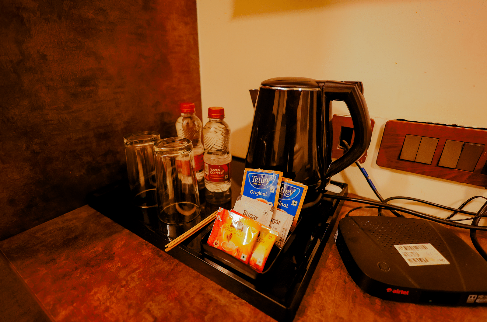 Close-up of amenities on a desk in a room at Nirantara Resort & Spa, Bengaluru, including a kettle, coffee, and a phone.