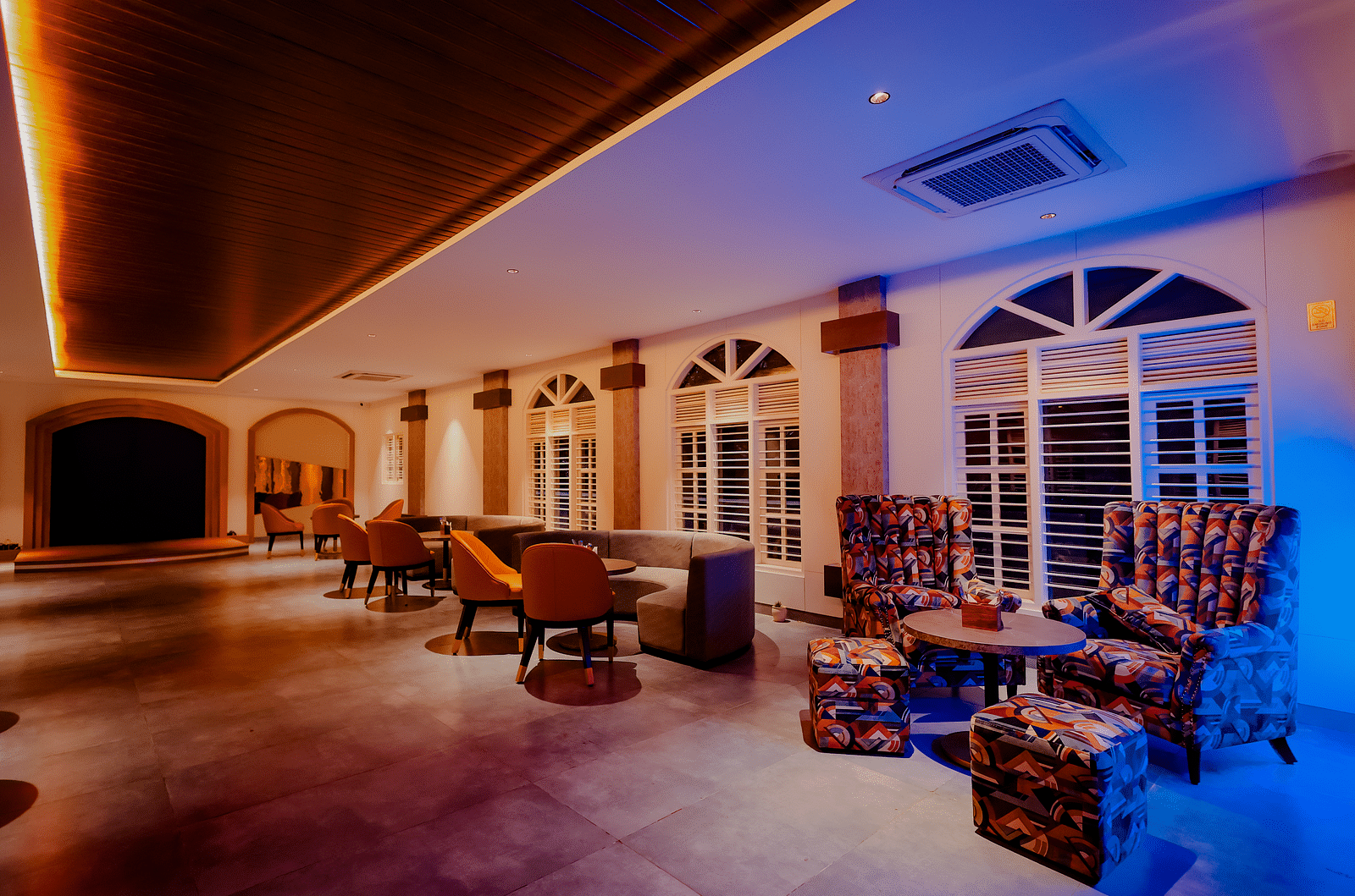 A spacious lounge area at Nirantara Resort & Spa with comfortable seating, decorative lighting, and a view of the outdoors.
