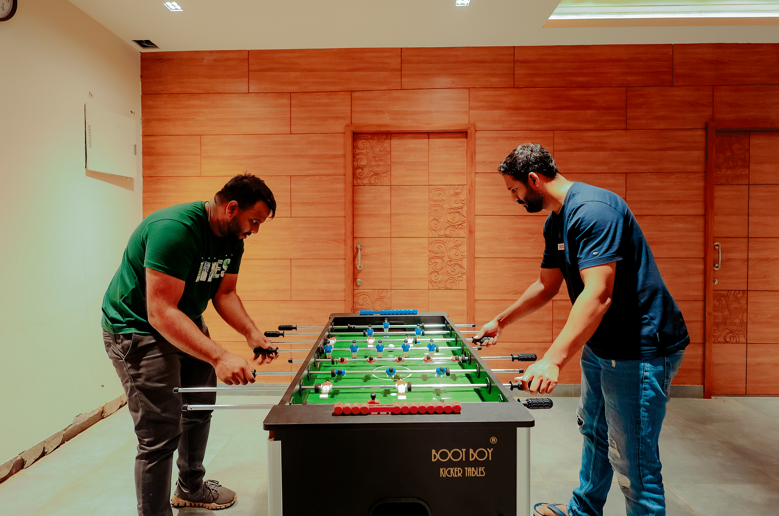 Two people playing foosball at Nirantara Resort & Spa in a room with wood-panelled walls.