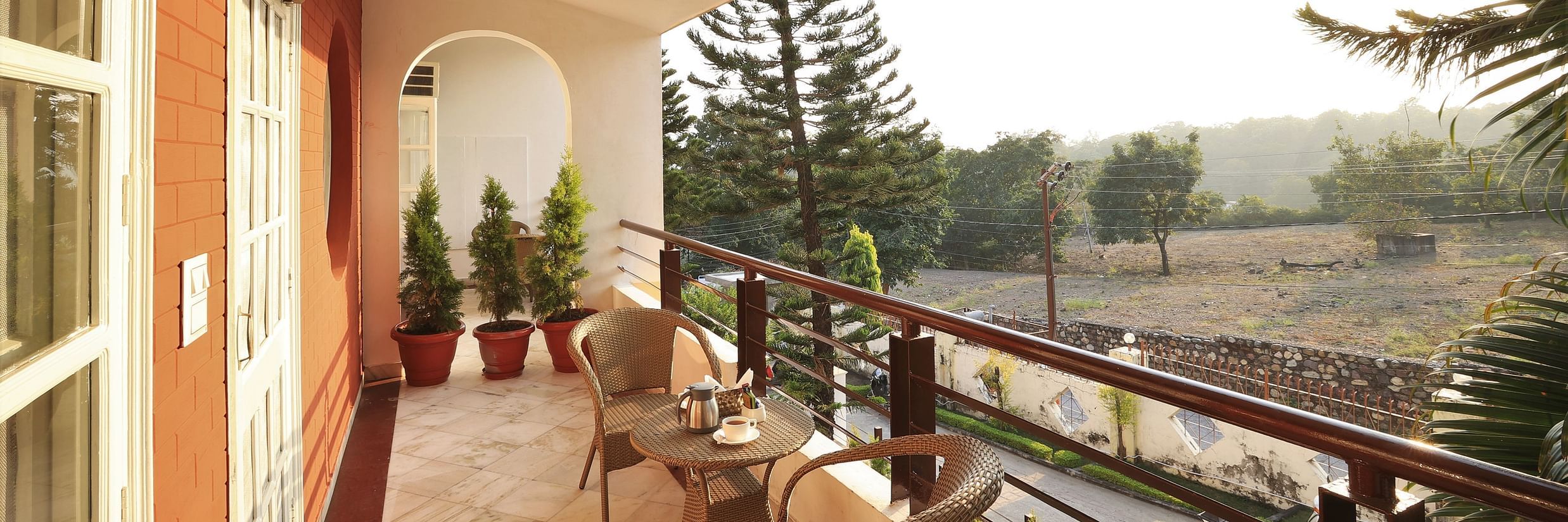 An image of a balcony where chairs are placed from where green trees and plants can be seen - Lamrin Boutique Cottages Rishikesh