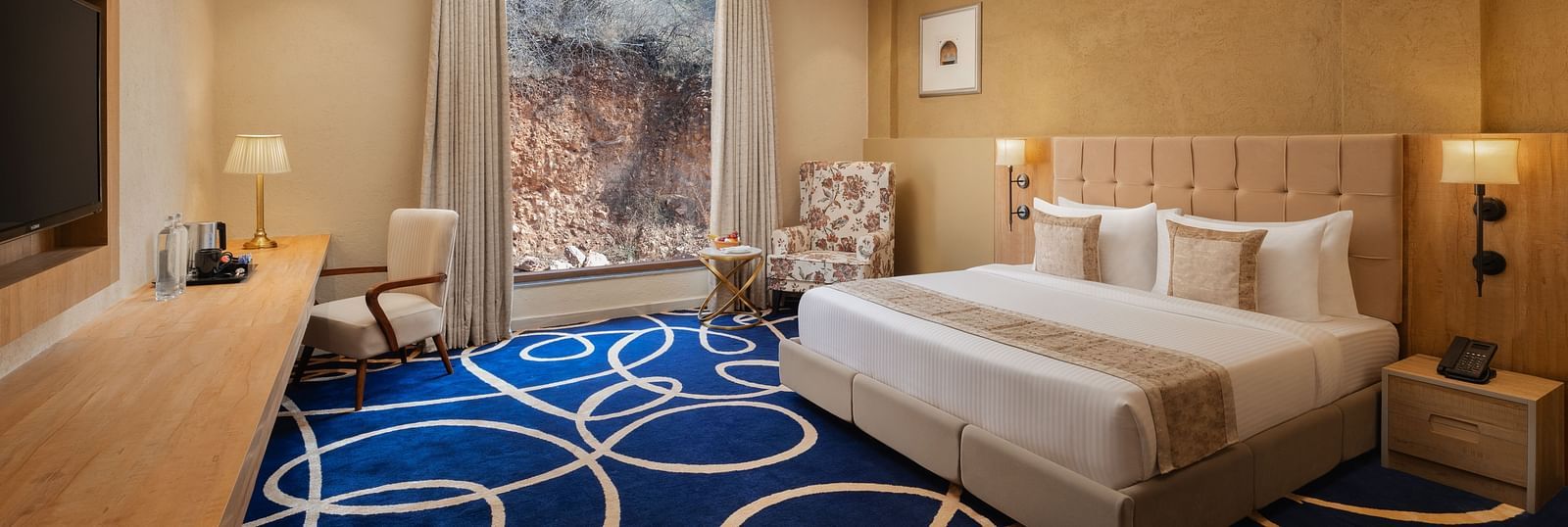Deluxe room with a king size bed placed in front of a TV at Essentia Luxury Resort & Spa, Udaipur.