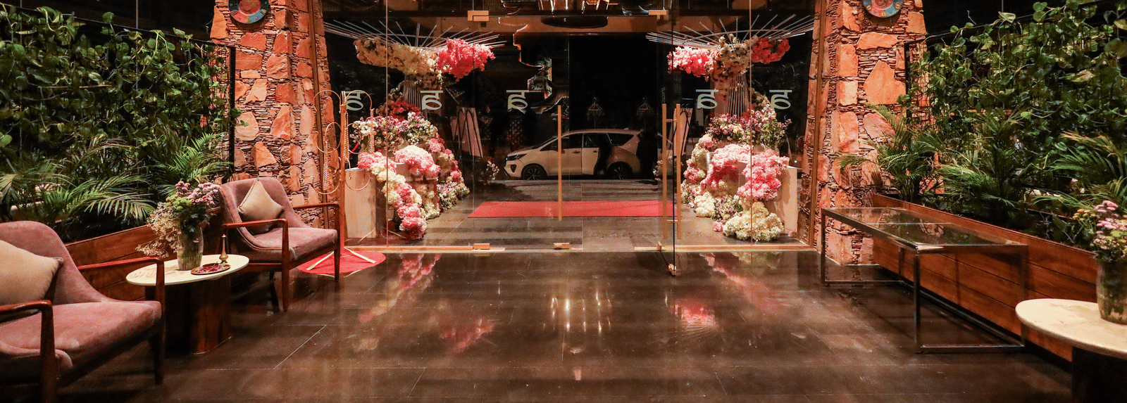 The interior entryway at Ananta Spa & Resort, Jaipur, features dark wooden floors, pink lounge chairs, and large pink floral decorations.