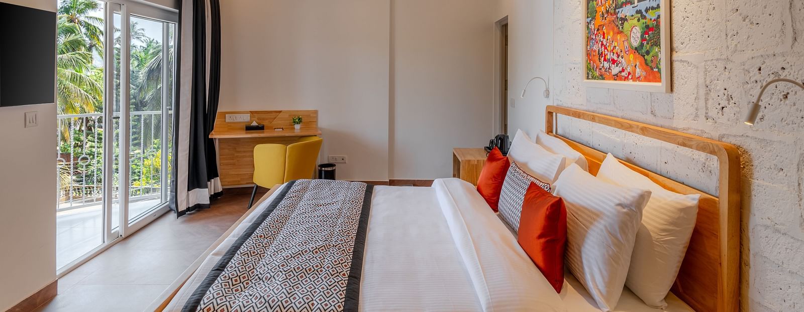 Bright hotel room with, flat TV screen, work desk and chair, vibrant art on the wall, and an access to the balcony at Bedzzz Xclusiv Morjim, Goa
