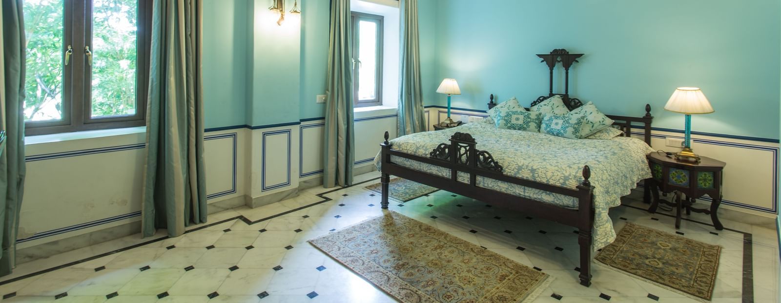 A spacious bedroom at Royal Heritage Haveli with a bed, seating area, ceiling fans, and light blue walls.