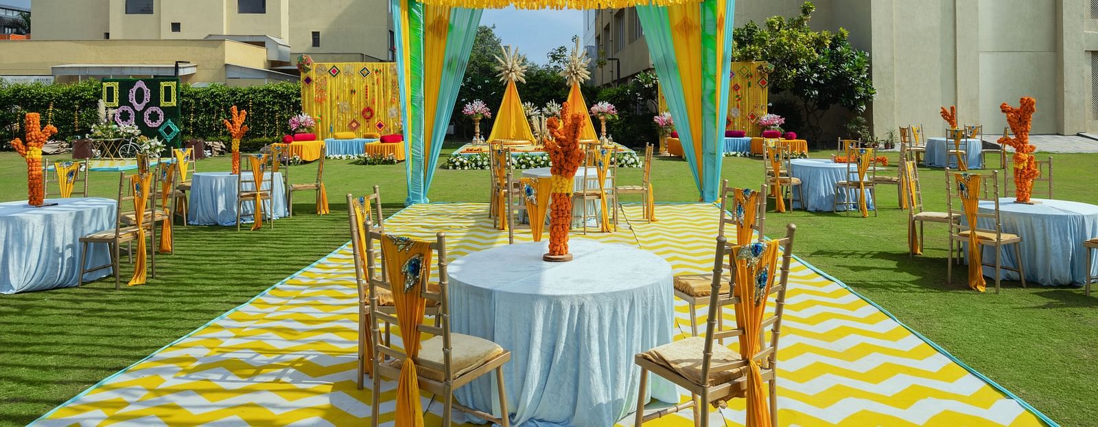 two tables with chairs in a cluster seated underneath a canopy during a sunny afternoon for shade - The Hideaway Banquets & Lawns, Greater Noida