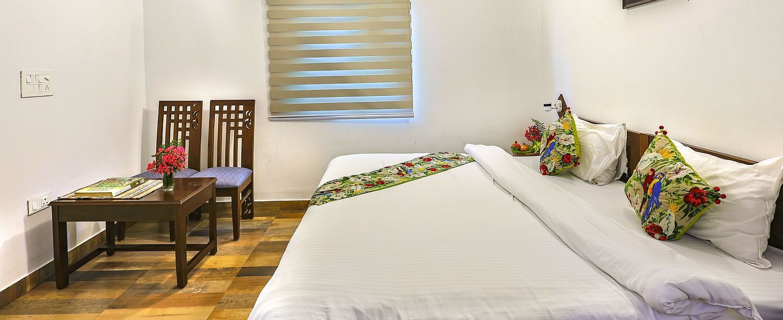 a double bed with a bed runner and chairs opposite it inside one of the rooms - Neer ganga Resorts