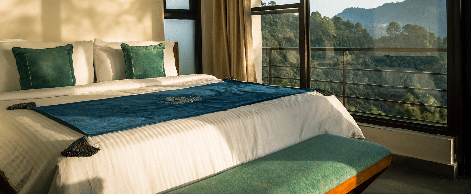 A bedroom with a balcony offering a mountain view and sunlight streaming in at BluSalzz Escapade Resort, Lansdowne