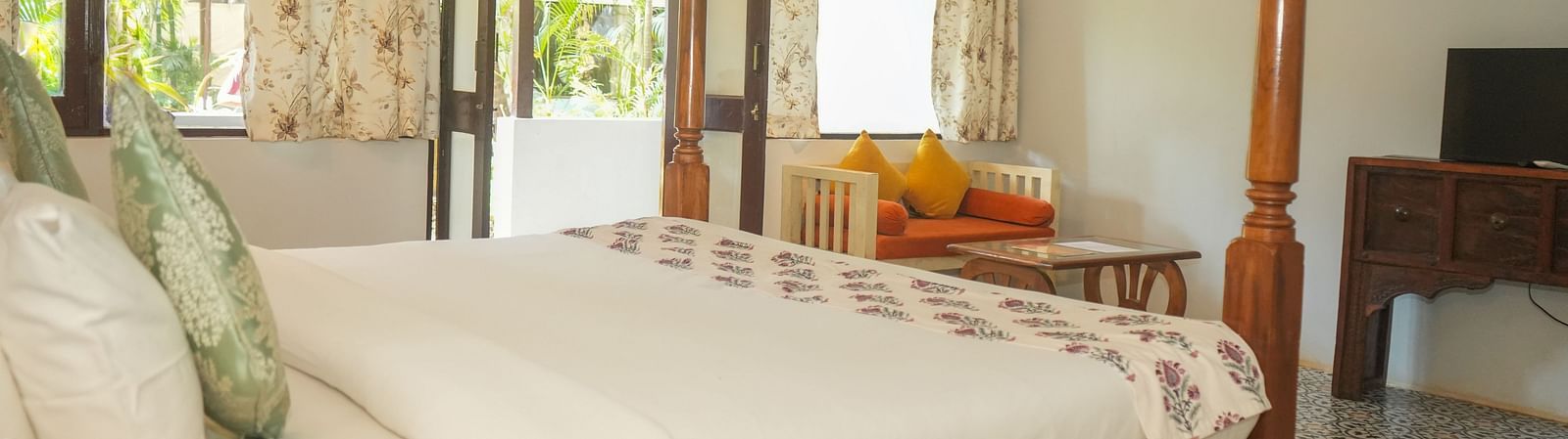 Side view of a canopy bed near large windows overlooking greenery at De Soul Santé, Morjim.