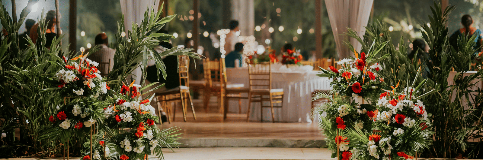 A beautifully decorated outdoor event space with white fabric draping, fairy lights, and large floral arrangements.
