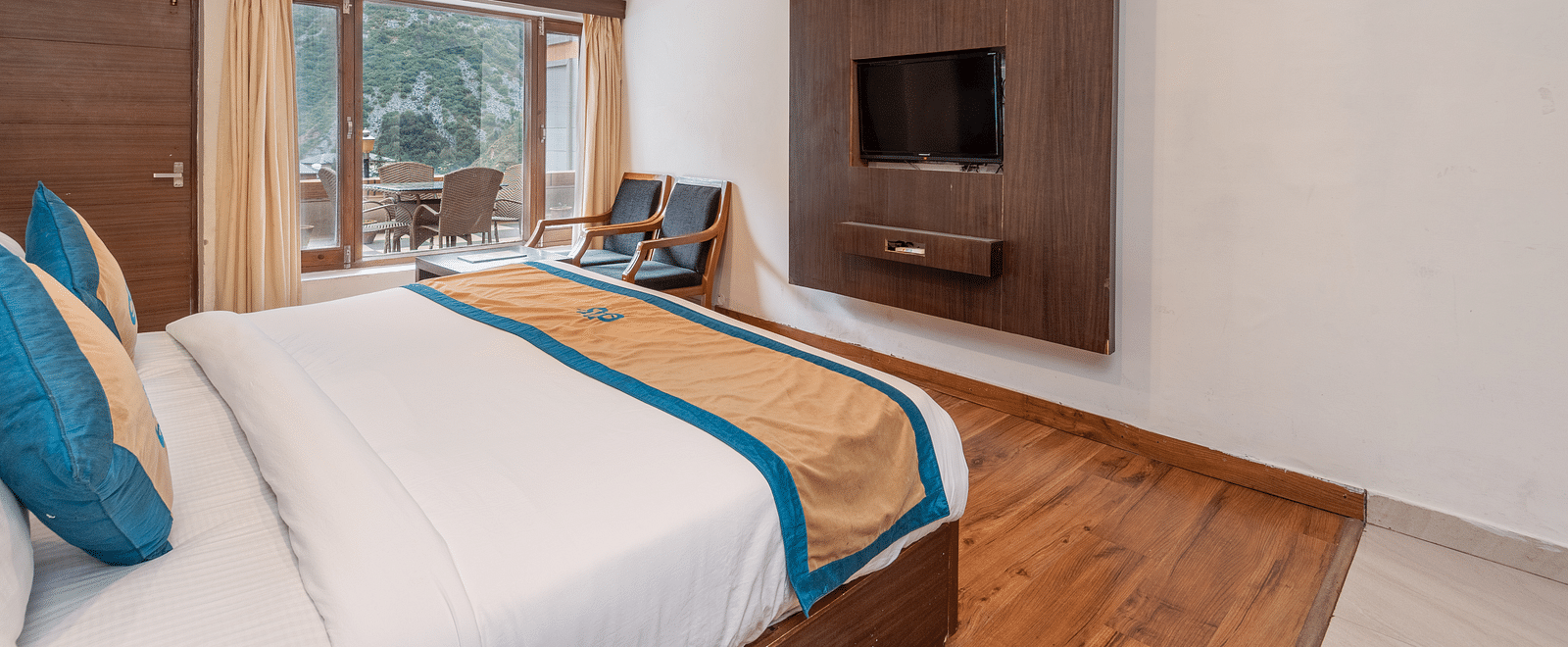 Side view of Premium Room at DLS Spring Valley Resort Dharamshala featuring a king size bed, chair and a balcony