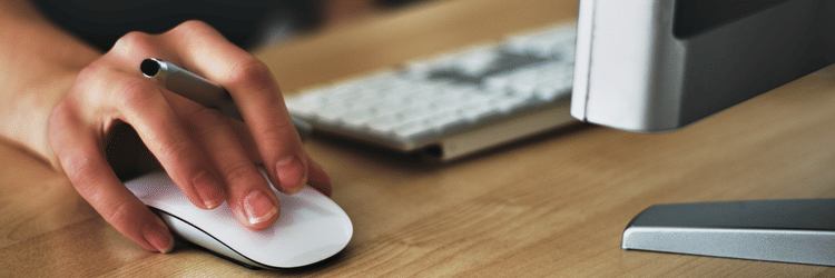 A hand using the mouse beside the monitor and keyboard.