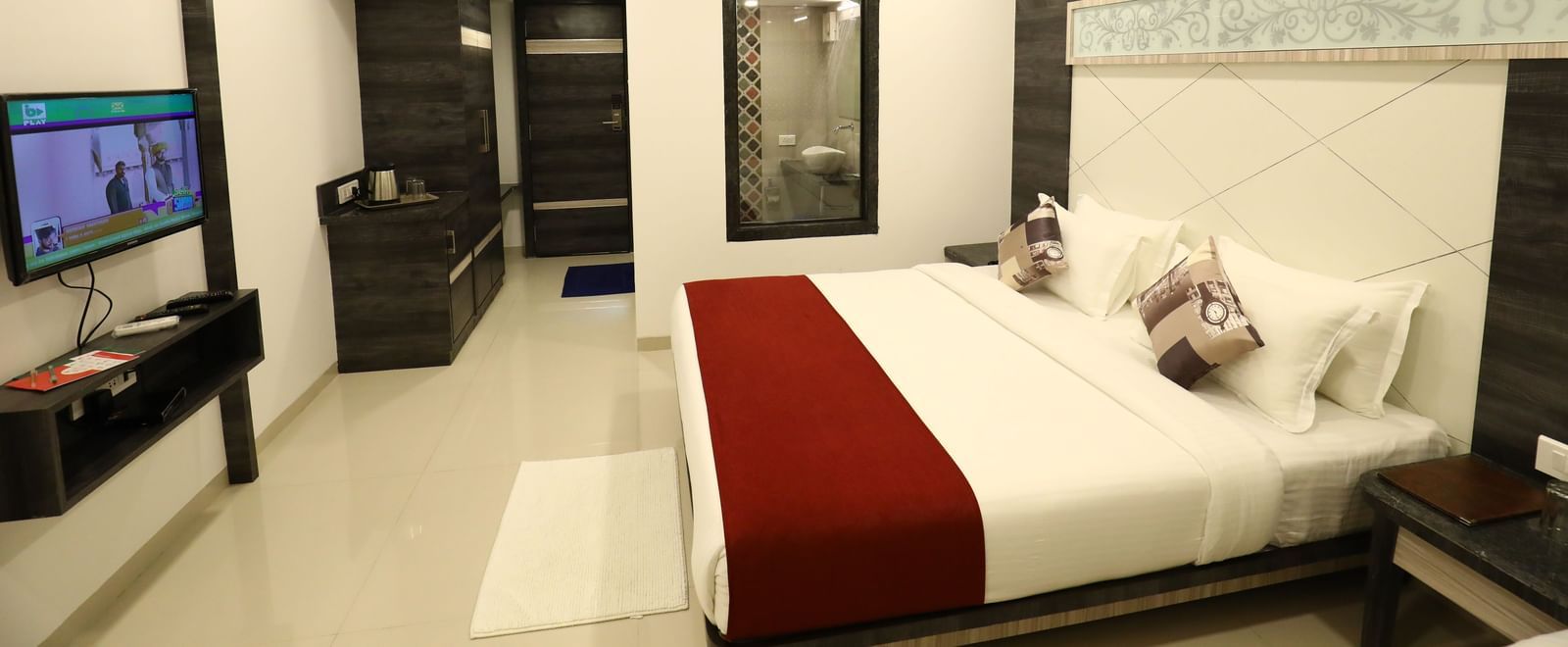A room in Imperial Grande with a bed covered in white and red bedding, a television on a stand, and a mirror on the wall.