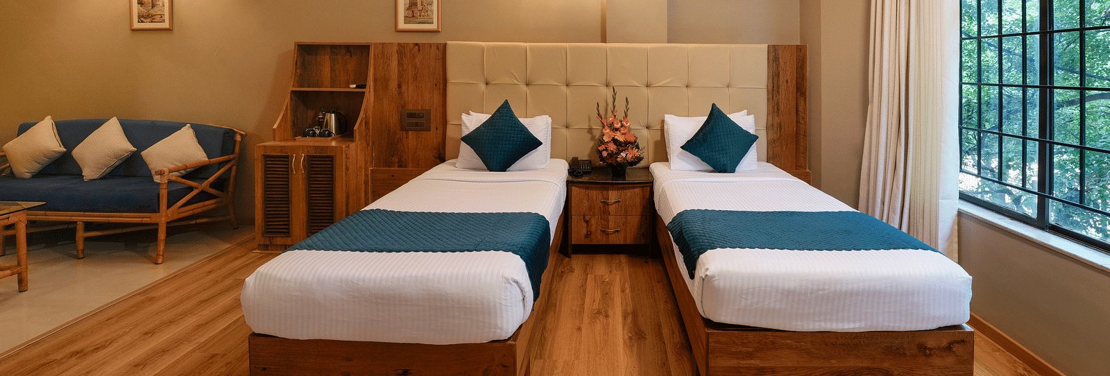 An image of a twin bed Deluxe Room with warm tones and modern amenities - Cross Roads Inn, Bengaluru