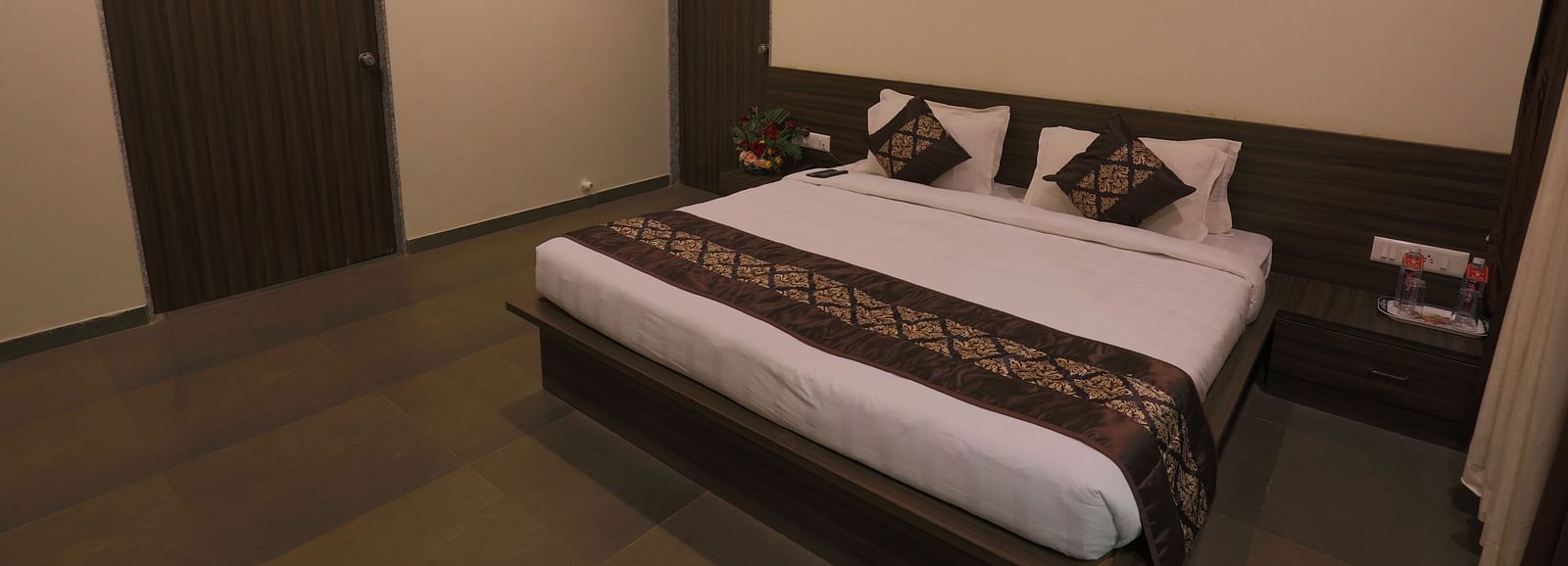 A bedroom with a double bed, dark wooden furniture, and a closed door - Vishal Lords Inn Gir Forest