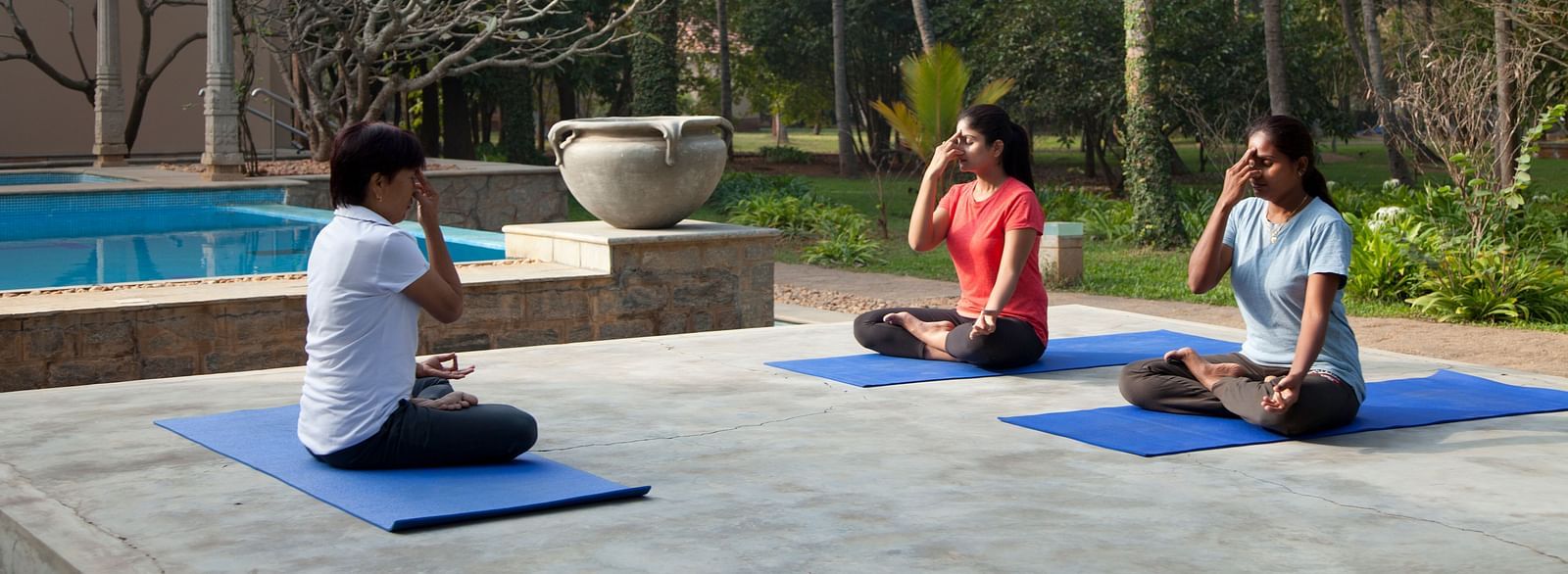 People doing yoga poses on mats by a pool, outdoor setting - Shreyas Retreat