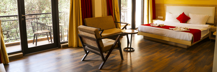 An overview of the Executive Suite with a double bed, chairs and balcony in view - Rosetum Anjuna.