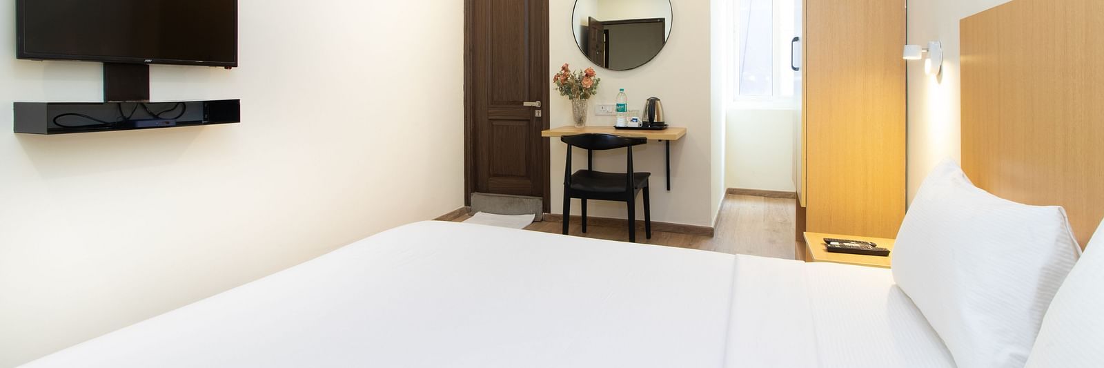 A bedroom with a double bed, white sheets, and a television on the wall - Sanctum Suites Richmond Road, Bangalore