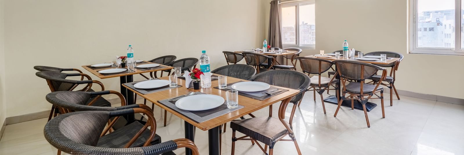 A dining area at Destino by Monday Hotels, Gachibowli, with 2 dining tables and woven chairs, set up with plates and water bottles.