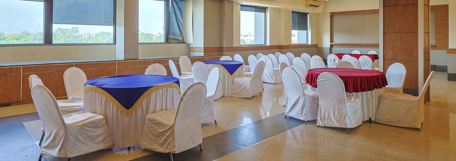 Banquet hall with white chairs, wooden ceiling and bright lighting at Max Hotel Prayagraj.