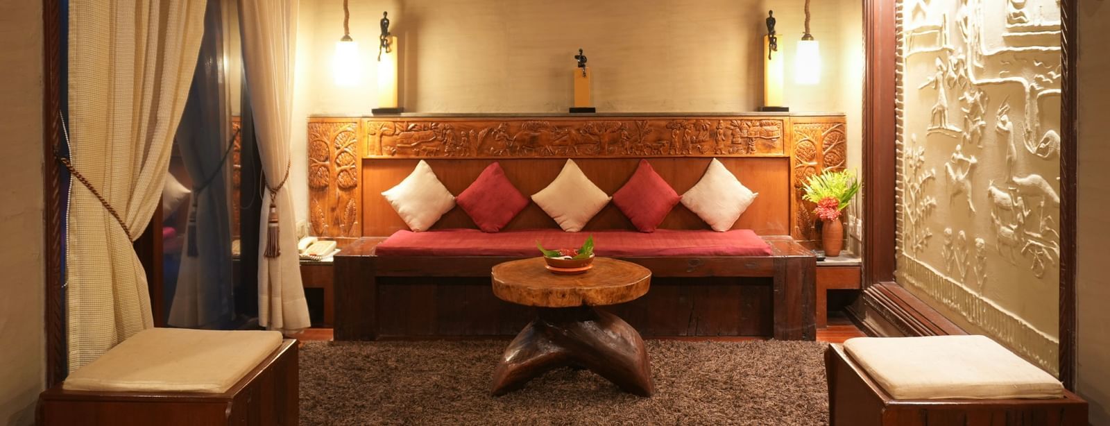 Warmly lit Zaminder Suite in Vedic Village Spa Resort featuring a separate living area with a wooden sitting area, carpeted flooring and intricate wall accents.