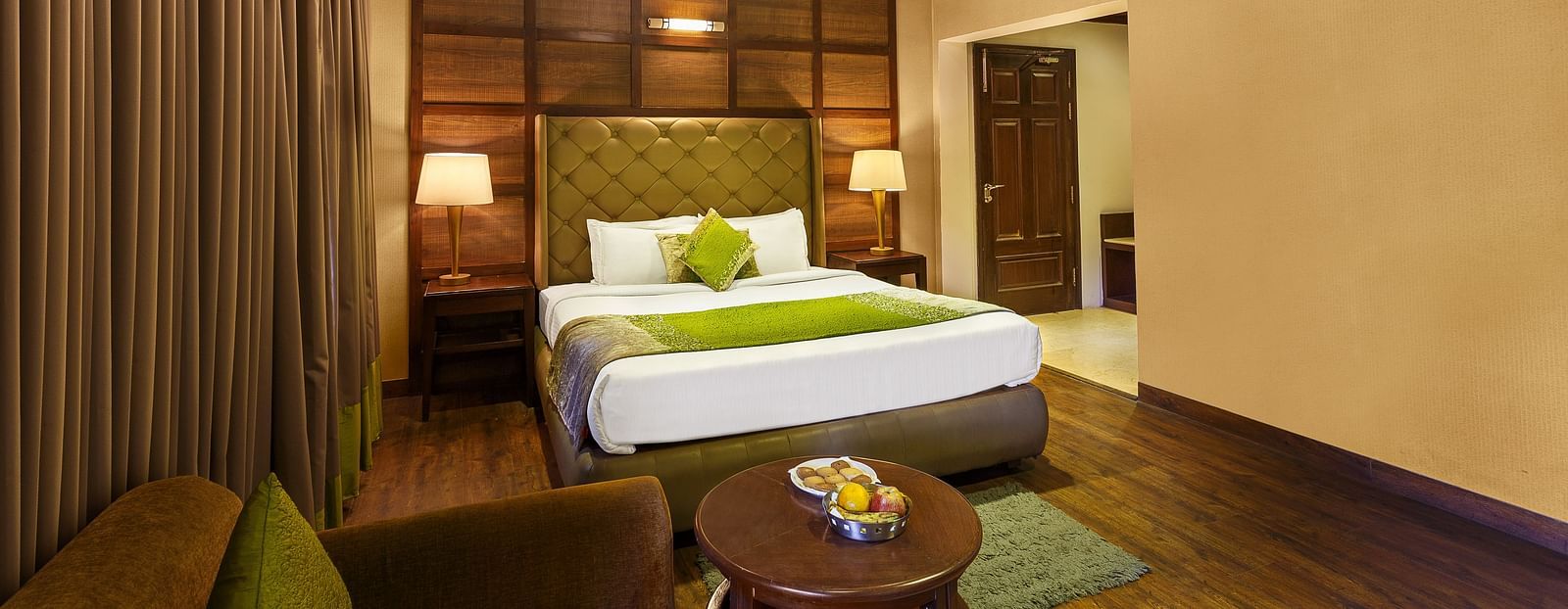 a bedroom with a large bed and side lamps, a table and a sofa - The Earl's Court, Nainital