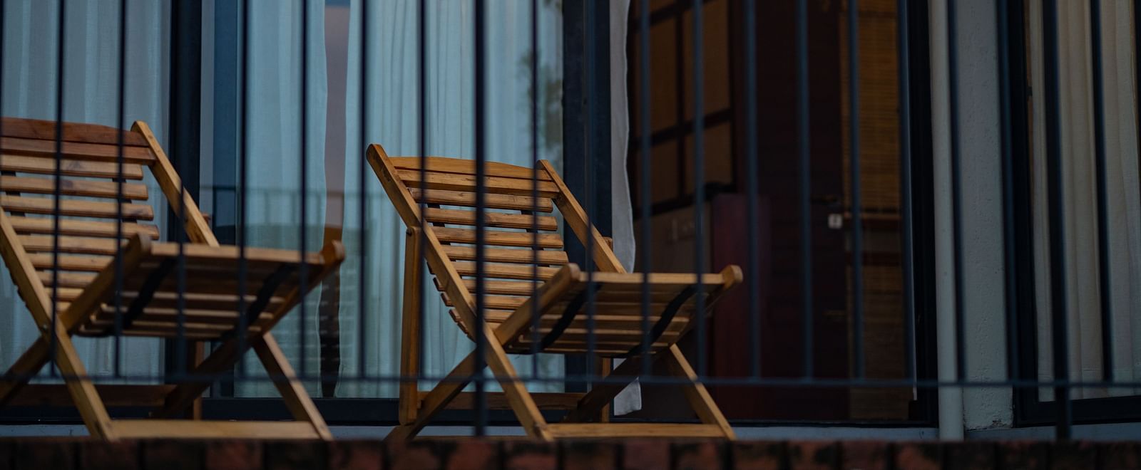  A private balcony at Vaasta Vagamon with two wooden lounge chairs, enclosed by a railing, offering a cozy outdoor seating area.