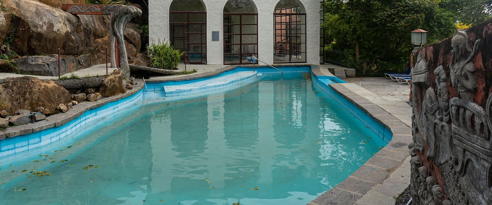 A white building with arched windows and a red roof next to a blue swimming pool at Mango Hill, Yercaud.