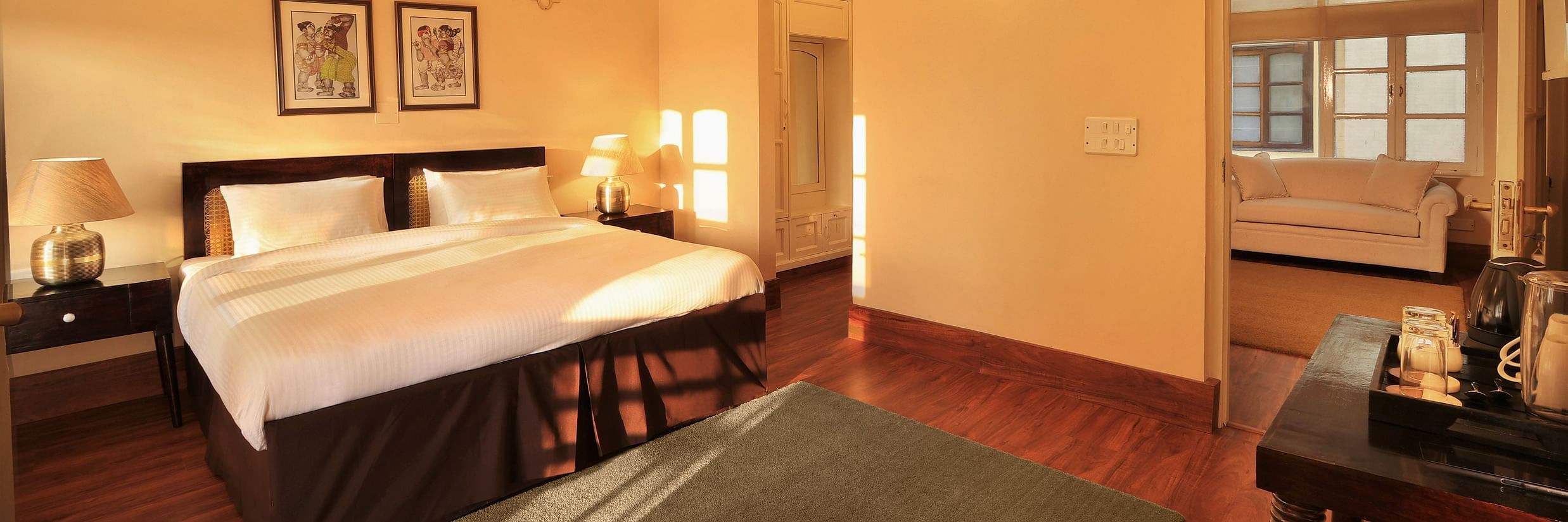 An image of a Super Deluxe room with a double size bed, bedside table with lamps on either side, and a table where antique and decorative items are placed - Lamrin Boutique Cottages Rishikesh