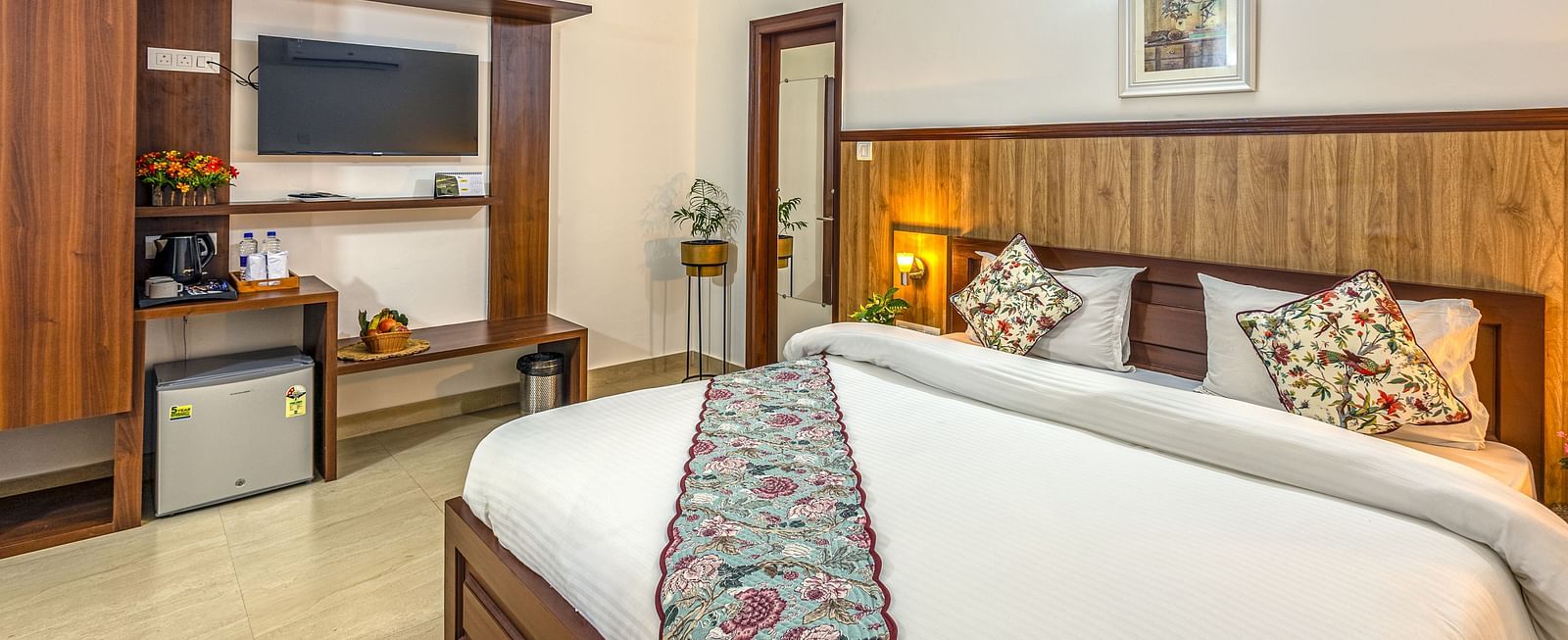 a double bed with side tables and lamps and a tv wall mounted next to it inside one of the rooms - Neer ganga Resorts