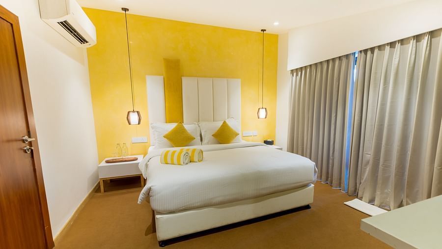 Pool Villa at Darza Resorts with a white bed, a bright yellow accent wall, and long grey curtains beside a large window. 