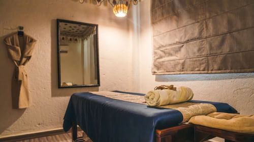 Spa table with a folded towel on top and a spa cloak hanging on the wall near a mirror.