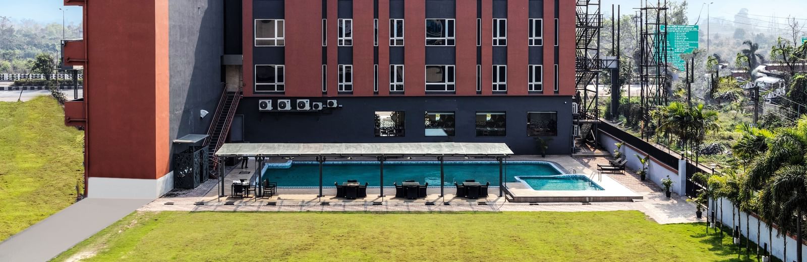 A modern hotel building with a swimming pool and green lawn under a partly cloudy sky | The Citi Residenci Hotel Banskopa
