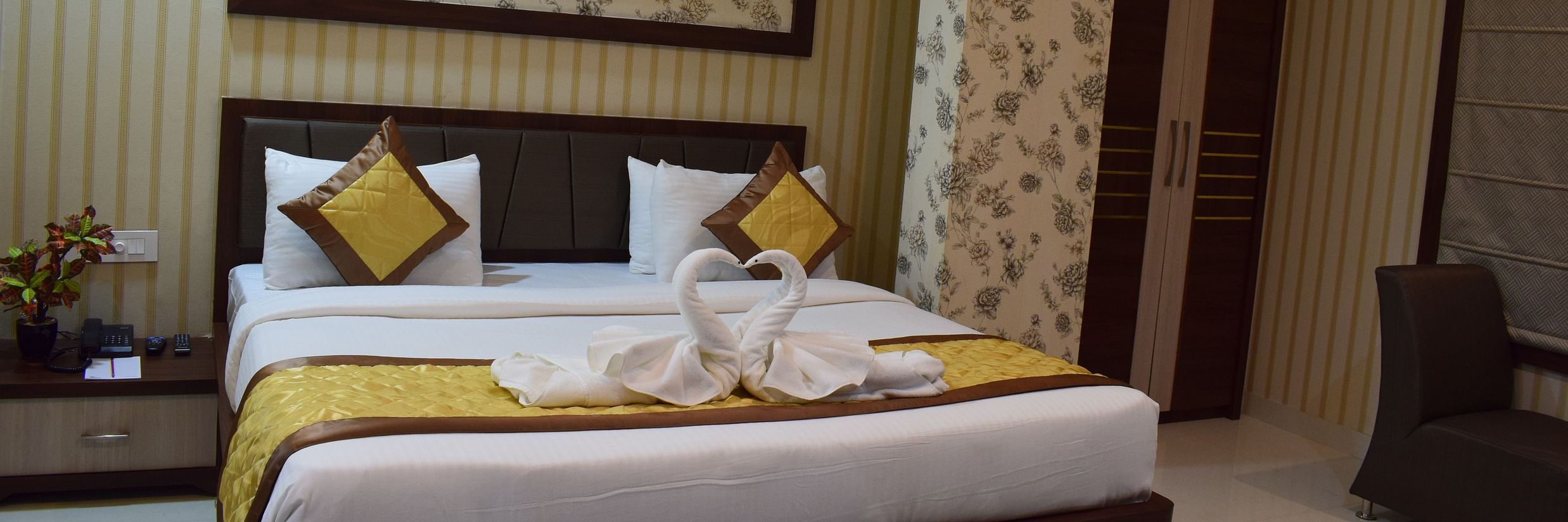 A spacious room featuring a neatly made large bed, chair, wardrobe and a bed side table at Hotel Uday Palace.