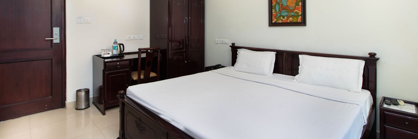 A room with a neatly arranged double bed, wooden furnishings, bedside tables, and a warmly lit lamp for a relaxing atmosphere at Sanctum Suites Indiranagar, Bangalore.