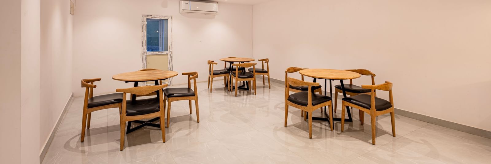 A brightly lit, minimalist dining or common area with several wooden tables and chairs arranged on a light-colored floor - Beestay Hotels Financial District, Hyderabad 