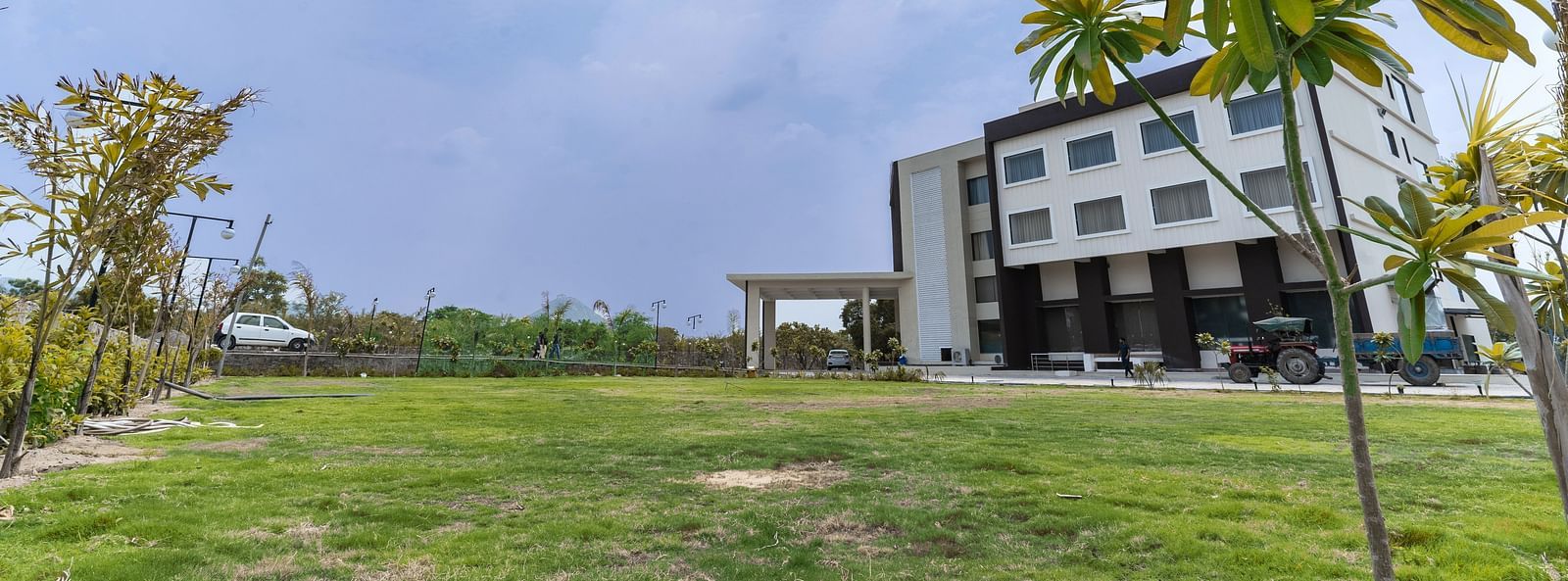 A wide-angle shot of a Bamboo Saa Mulberry Resort, Pushkar with palm trees and a lawn in front of it.