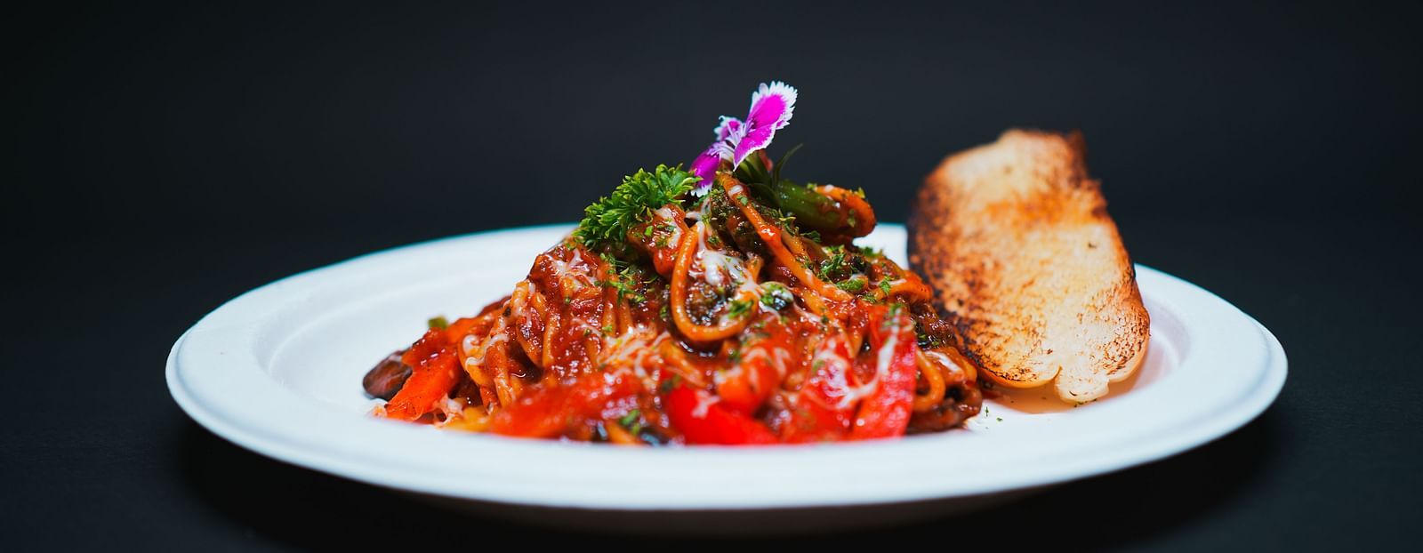 A gourmet pasta dish topped with rich tomato sauce, herbs, and an edible flower, served with a bread roll at D Café in Dip Holidays.