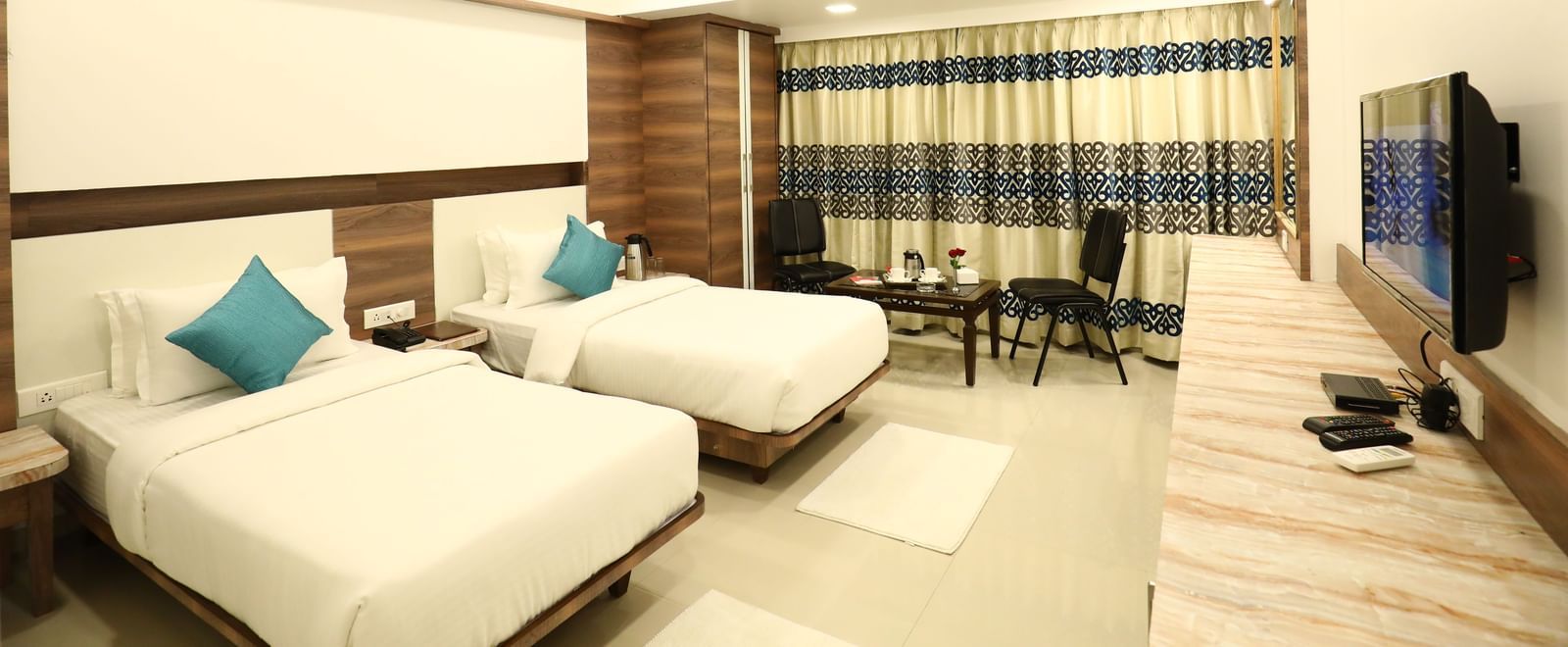 A spacious room in Imperial Grande with twin beds, a wall mounted television, and patterned curtains on the windows.