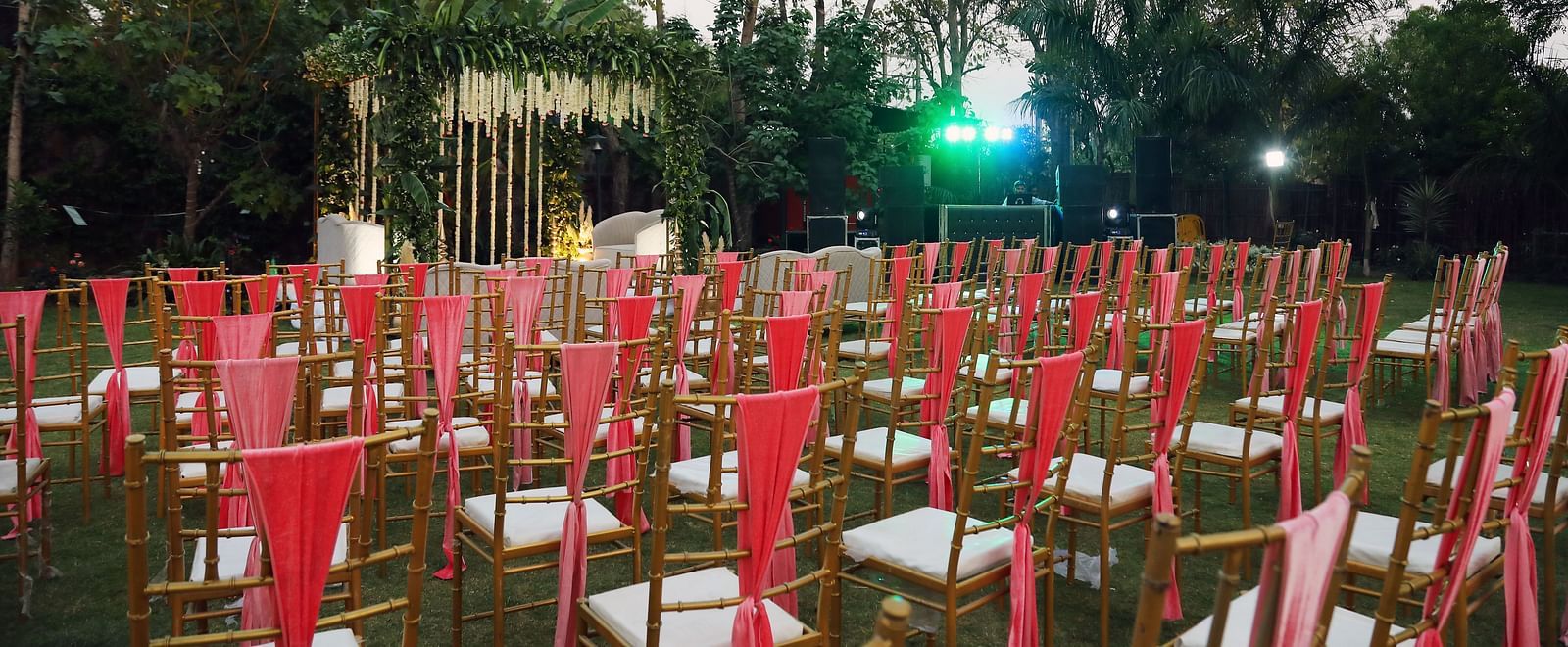 Outdoor seating arrangement at Tisya Farms, Gurgaon with rows of red chairs on grass facing a stage.