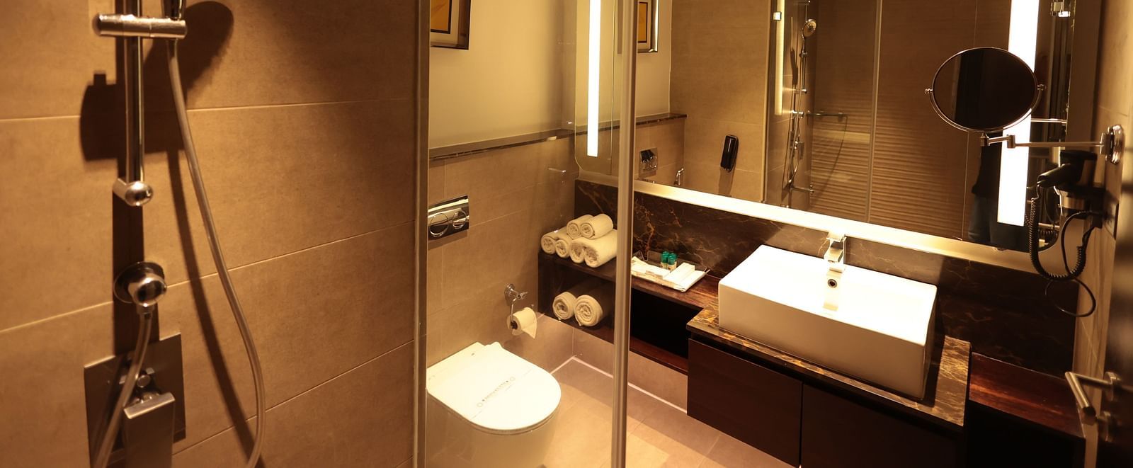 A spacious washroom with a glass panel separating the shower area from the Western toilet and a washbasin below the wall-mounted mirror | Cenneys Gateway