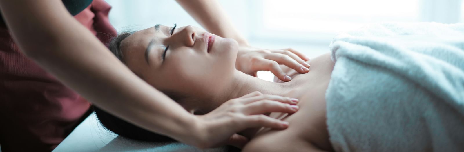 A young woman with her eyes closed is receiving a relaxing neck and shoulder massage from a masseuse.