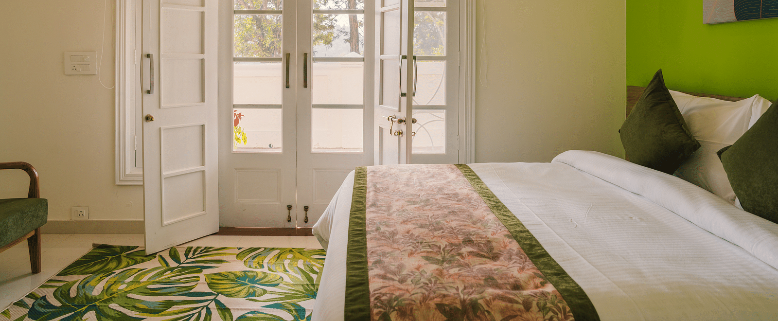 A side view of the neatly made bed with a carpet on the floor and a pair of glass-panel doors leading to the balcony at  BluSalzz Villas - The Green Roof, Bhimtal.
